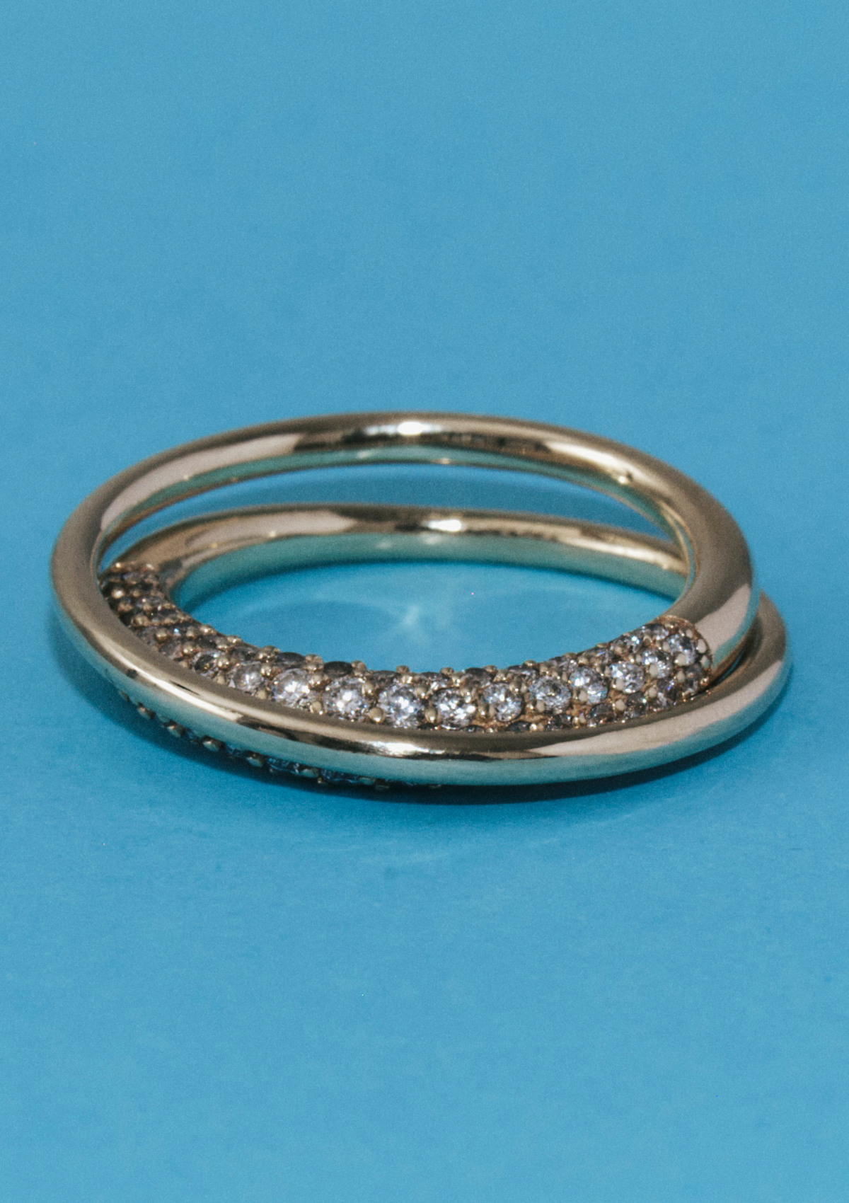 close up of sculptural infinity loop gold ring with pave diamonds on a blue background
