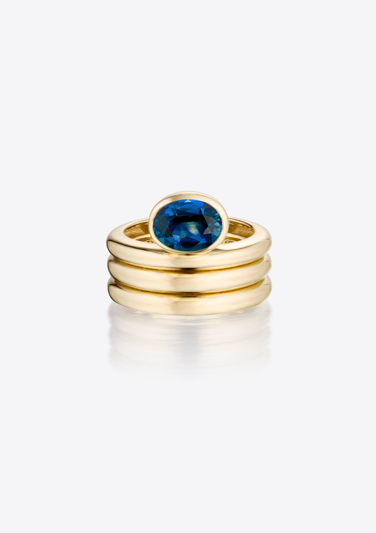 Sculptural, gold ring with a triple ribbed band and an oval blue sapphire on a grey background