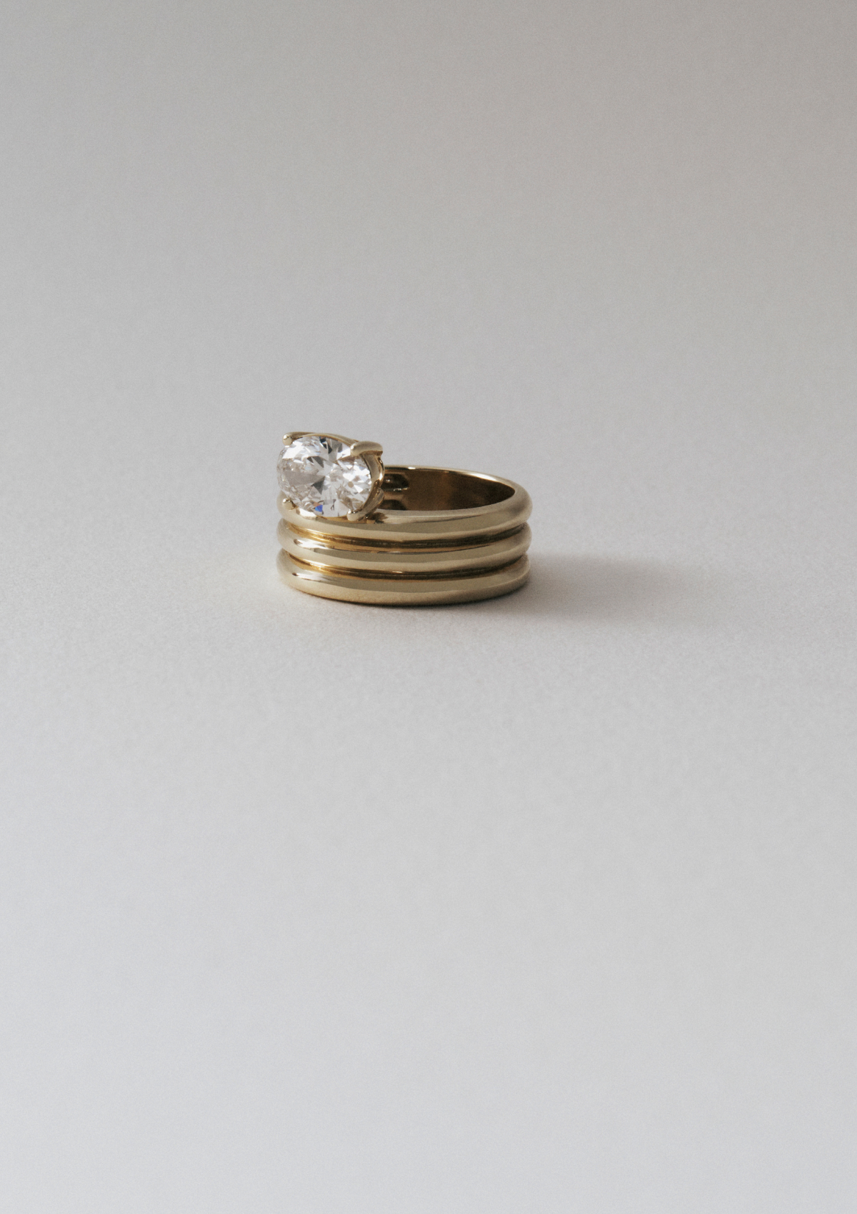sculptural ring with gold ribbed band and oval diamond. against a grey background