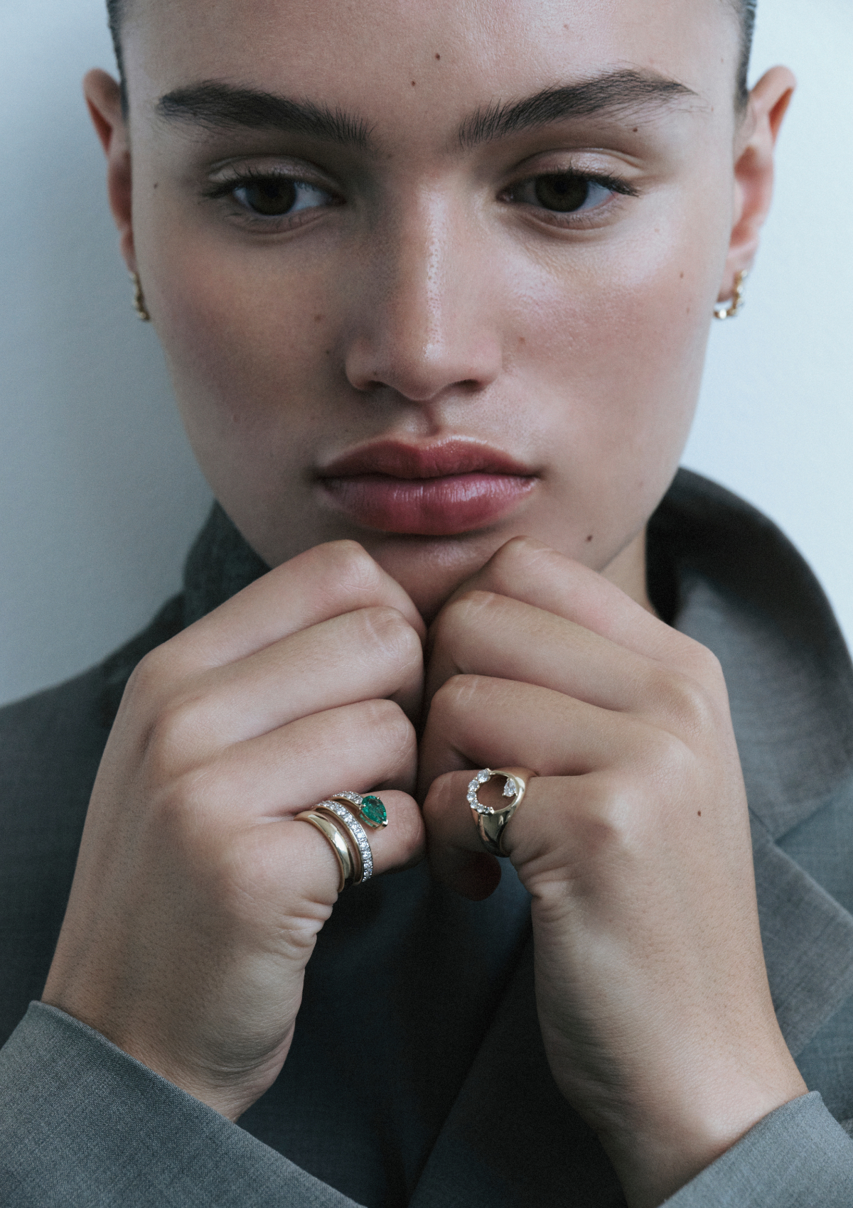 Close-up of a person wearing two rings. one of the rings has diamonds in pear and round shapes. the other has an emerald