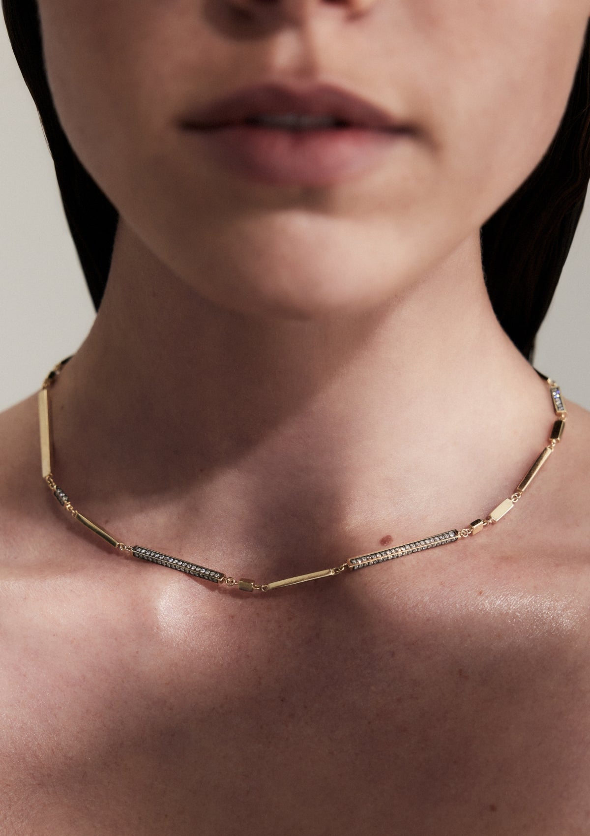 Close up of a woman's neck with a gold necklace that has uneven bars and round diamonds.