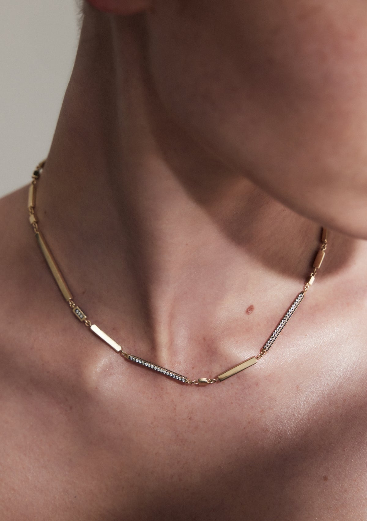Close up of model with a diamond necklace made with different sized bars of gold, sitting sculpturally uneven on the neck
