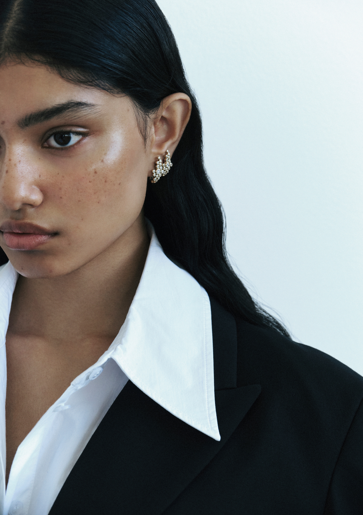 A woman wearing gold hoop climber earrings with small diamonds clustered together in a sculptural design