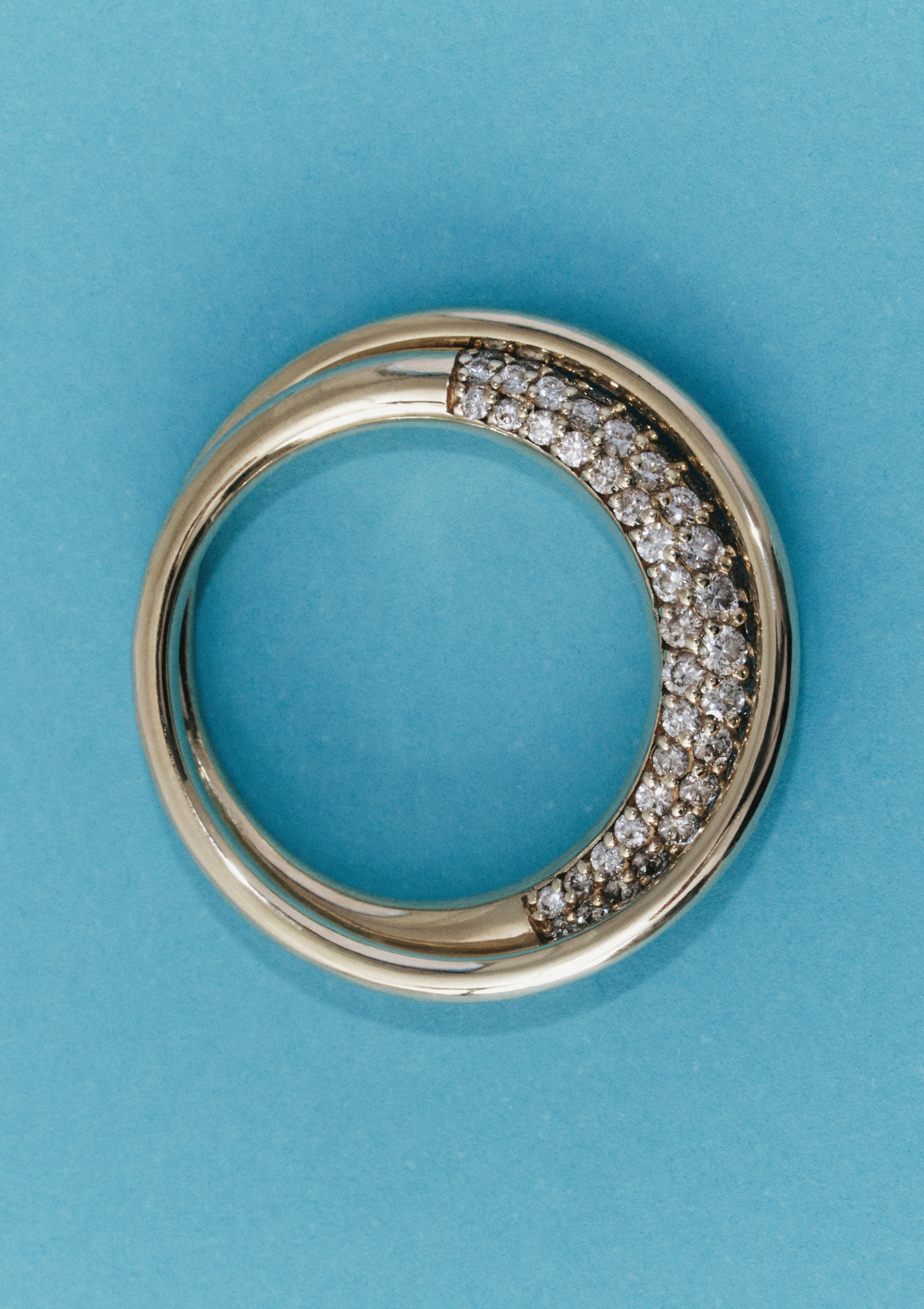 close up of gold sculptural infinity loop ring with pave diamonds on a blue background