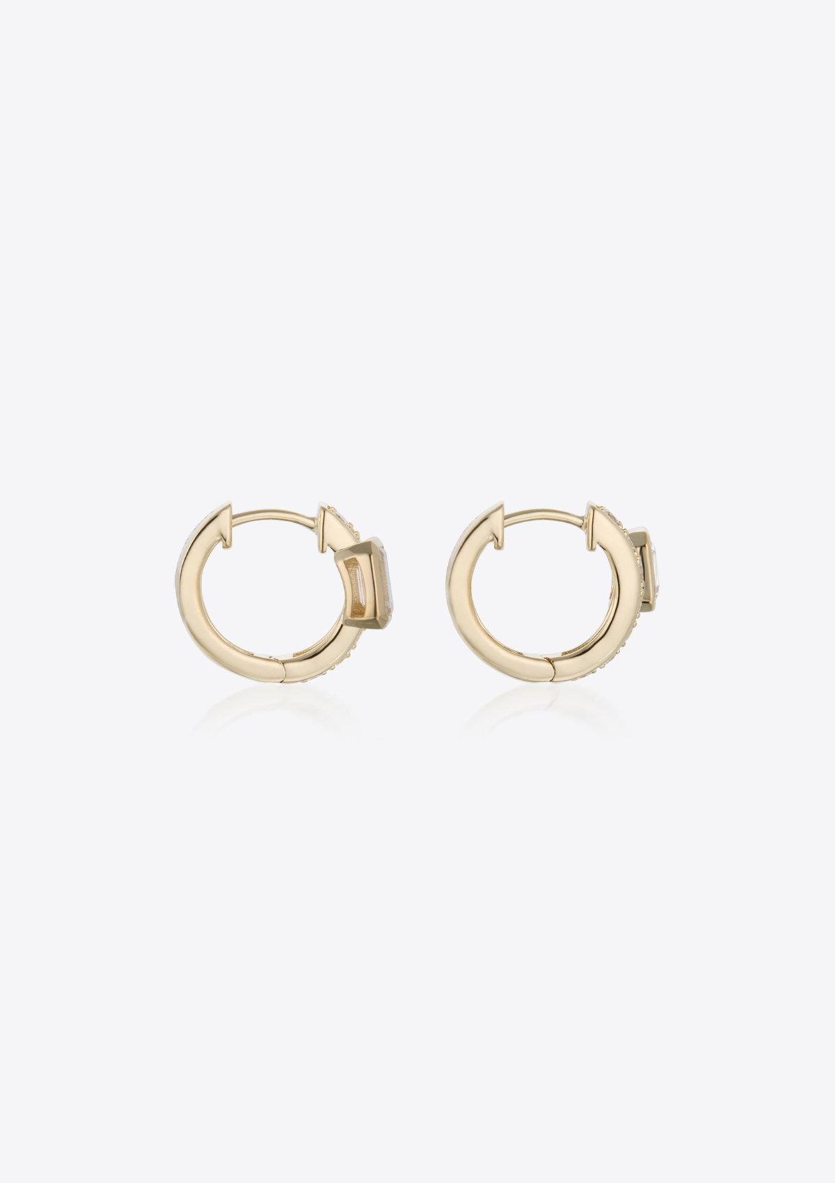 side view of yellow gold diamond huggies with emerald-cut diamonds placed off-centre on grey background
