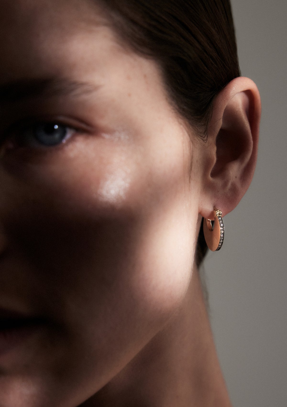 Close-up of a person wearing a pair of gold and diamond solid hoop earrings