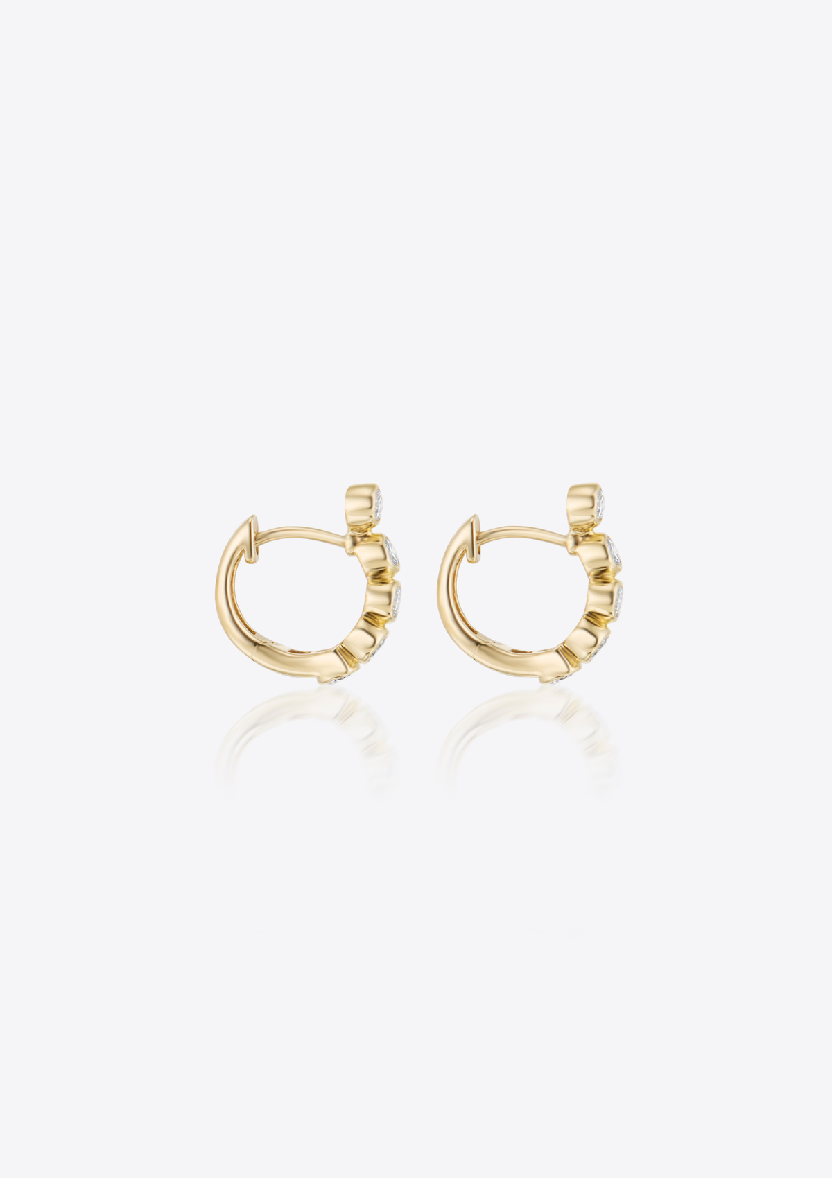 Gold earrings with small bezel-set diamonds shaped in a curve on a grey background. front view