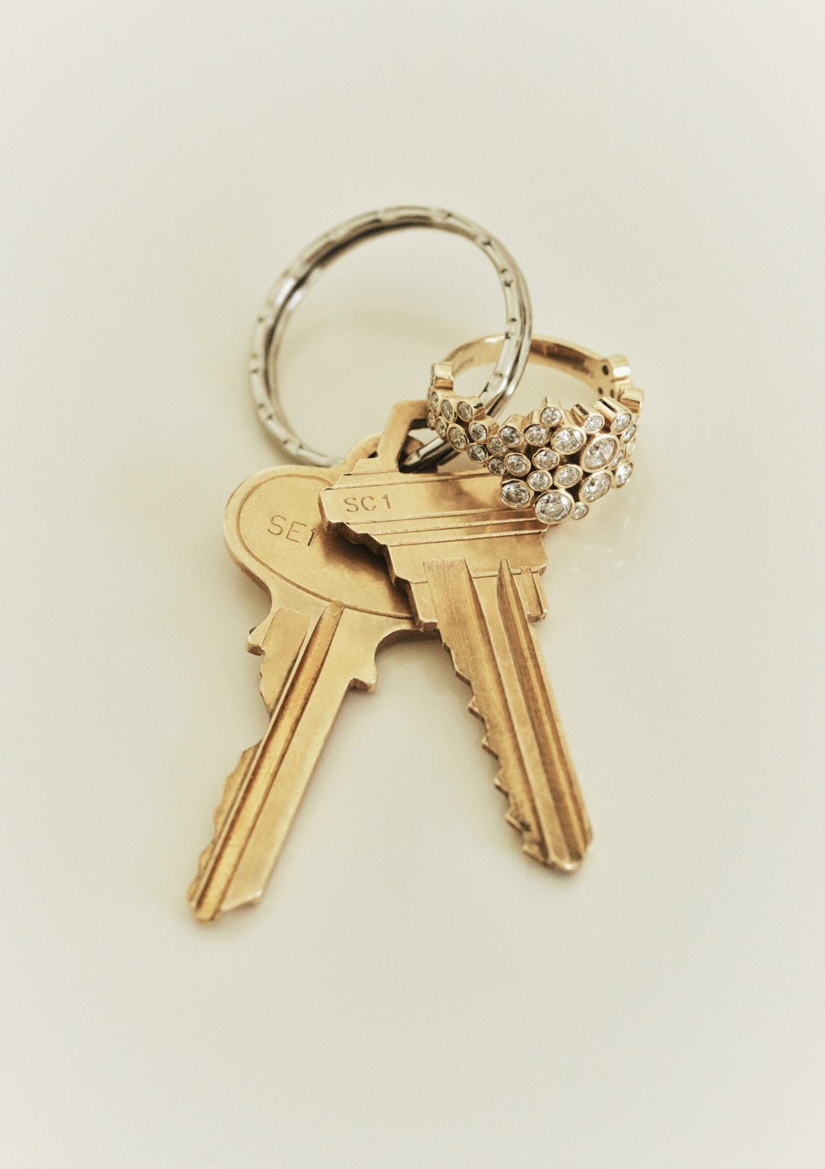 A close-up of a keyring with two gold keys attached and a ring with various small diamonds, shown on a plain light background.