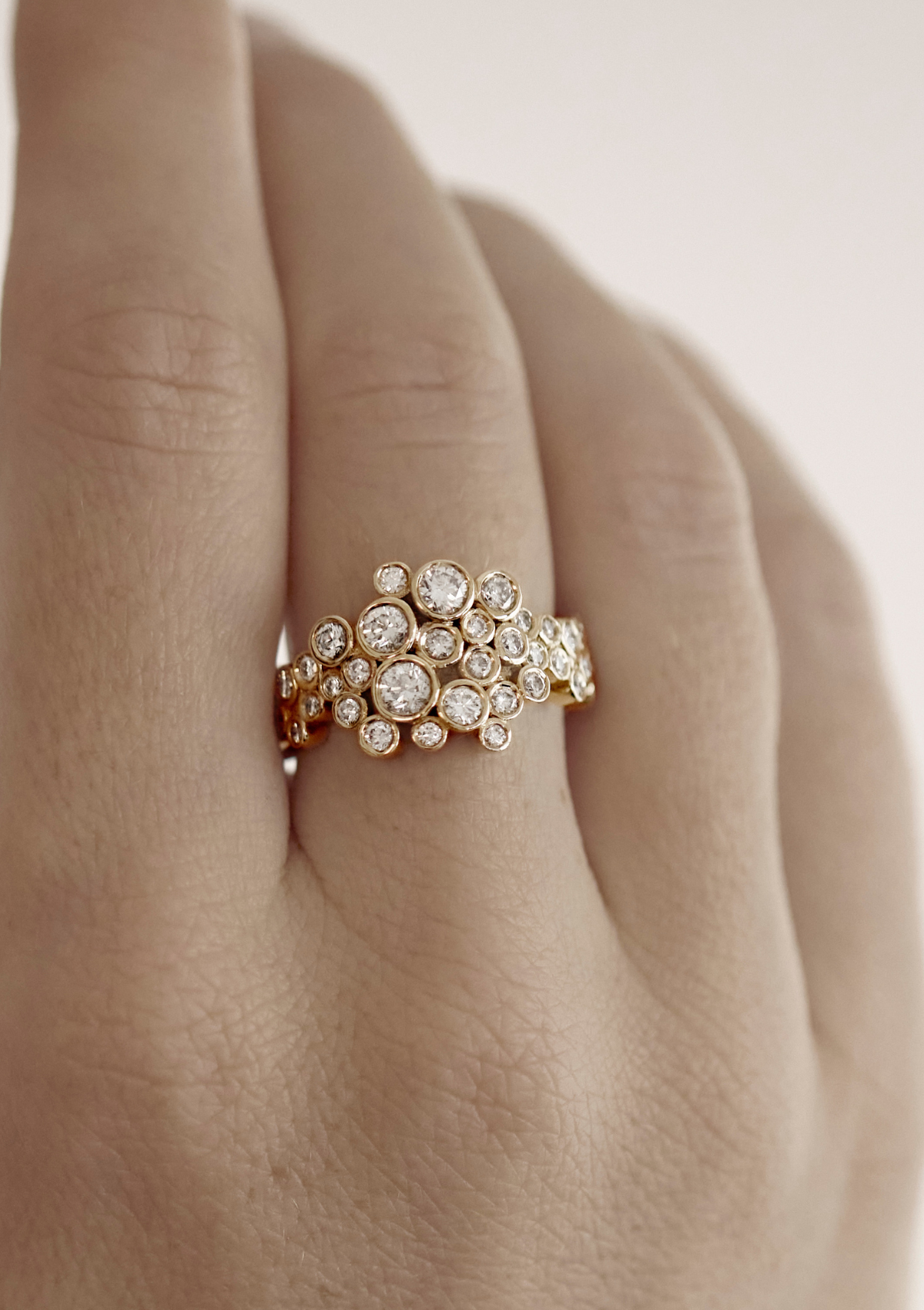 Gold ring with diamonds on a finger against a neutral background