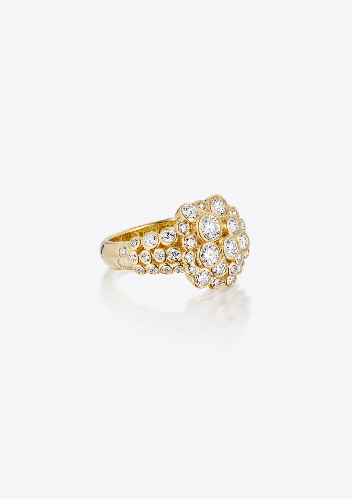 A gold ring featuring a large, round cluster of diamonds on the band, photographed against a grey background with a soft reflection.