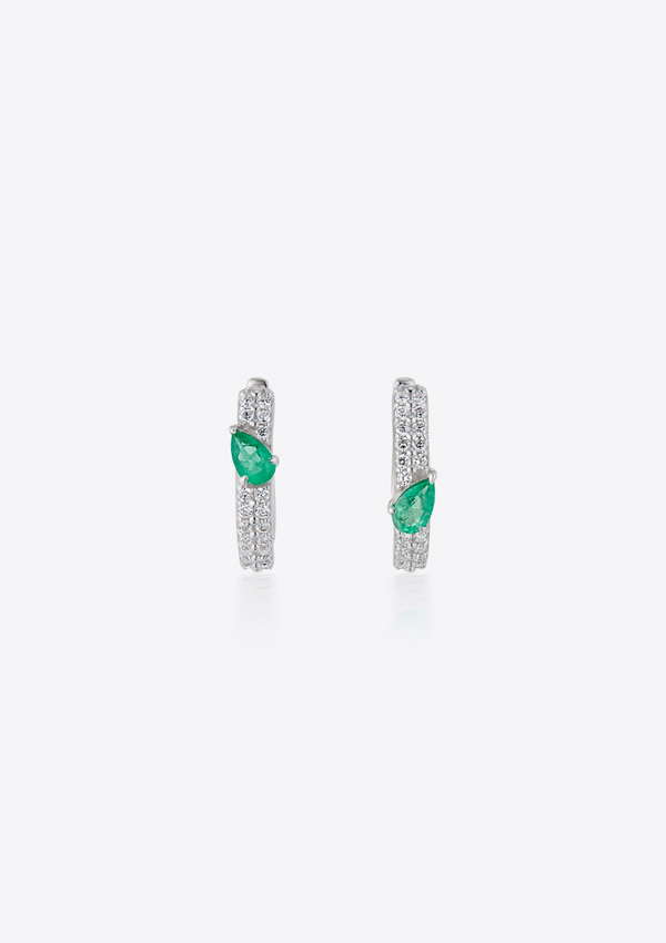 Pair of pave diamond earrings with pear-shaped emeralds asymmetrically positioned. against a grey background