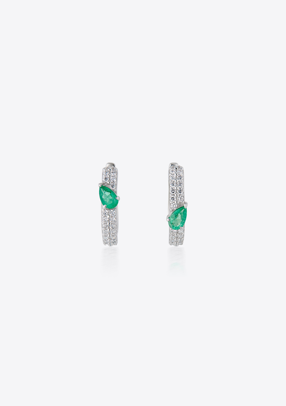 Pair of pave diamond earrings with pear-shaped emeralds asymmetrically positioned. against a grey background