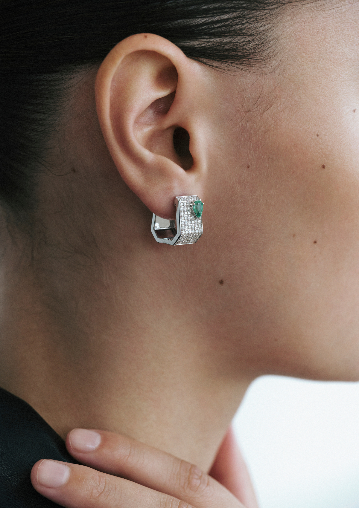 Close-up of a geometric shaped earring with diamonds and emeralds worn by a woman