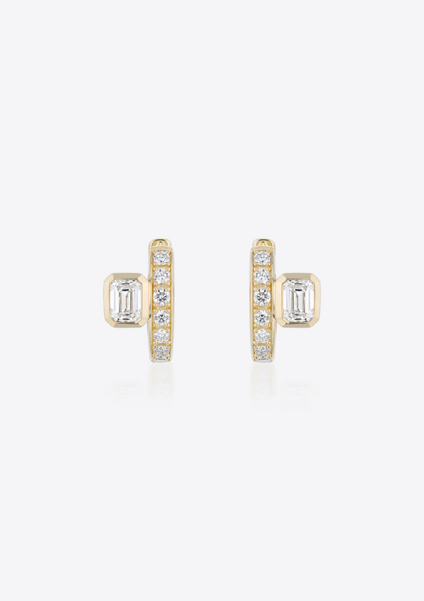 front view of yellow gold diamond huggies with emerald-cut diamonds placed off-centre on grey background
