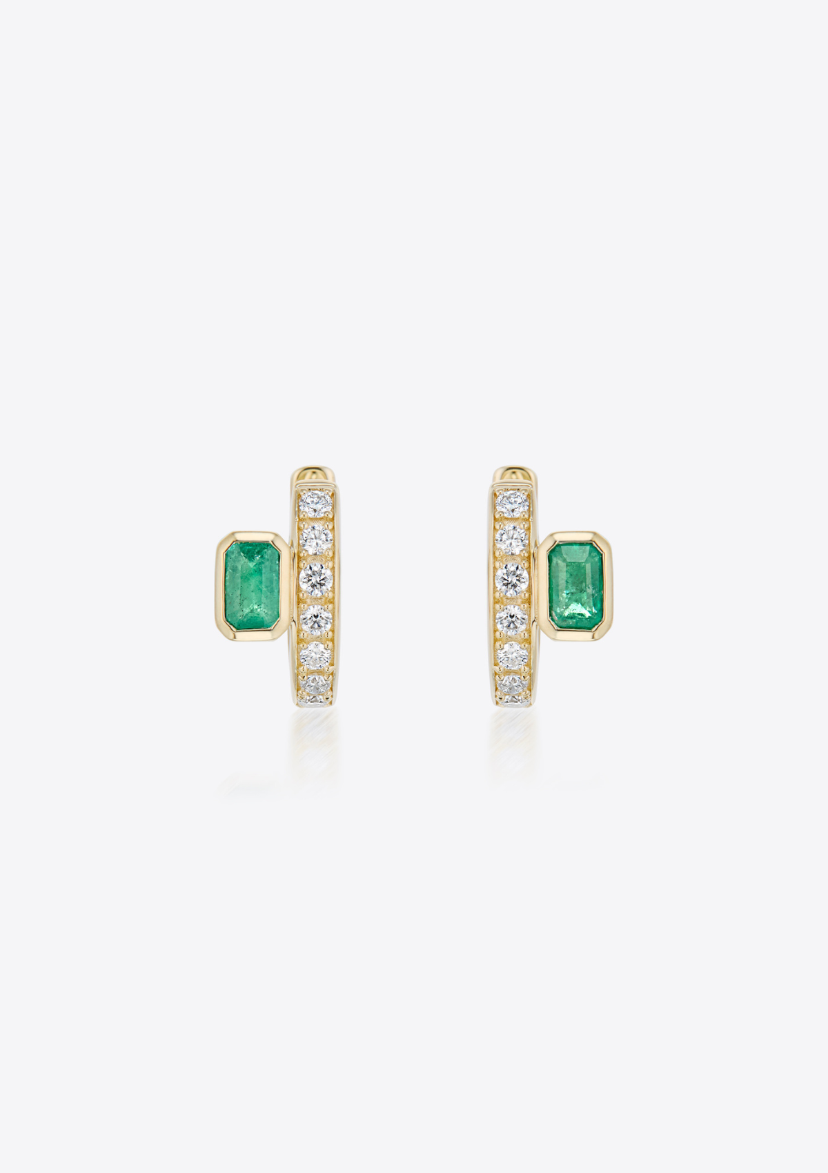 Front view of a pair of gold diamond huggies with emeralds placed off-centre on a grey background