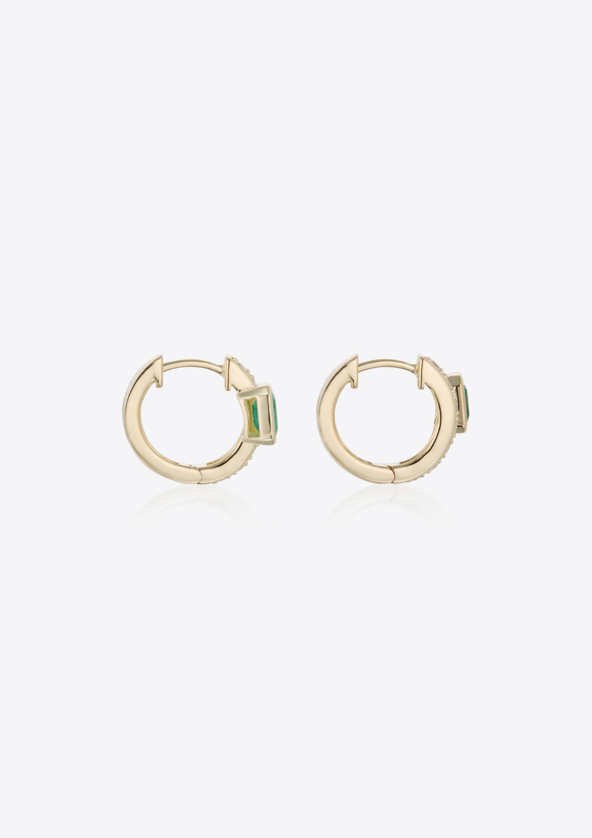 Side view of gold diamond huggies with emeralds placed off-centre on a grey background
