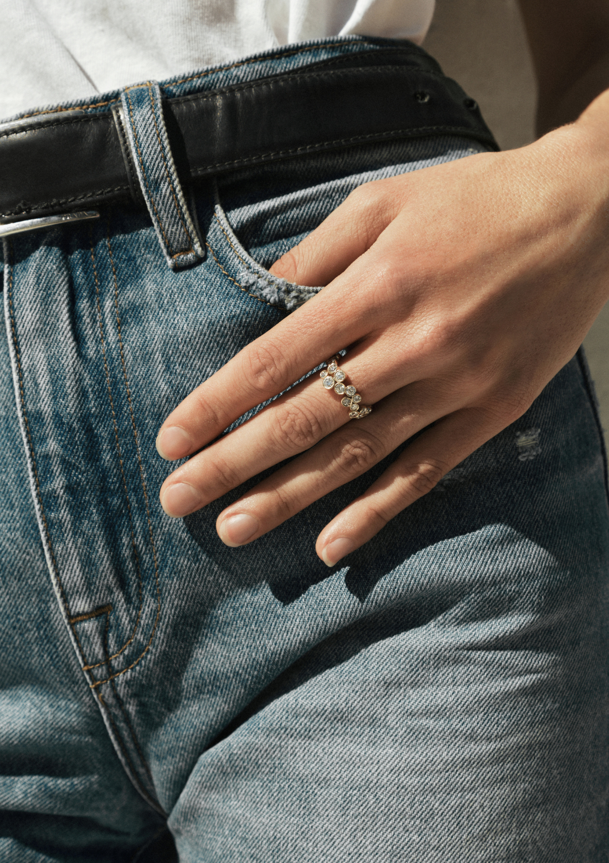 A close-up of a person's hand resting on blue denim jeans, wearing a gold ring with scattered diamonds in different sizes.