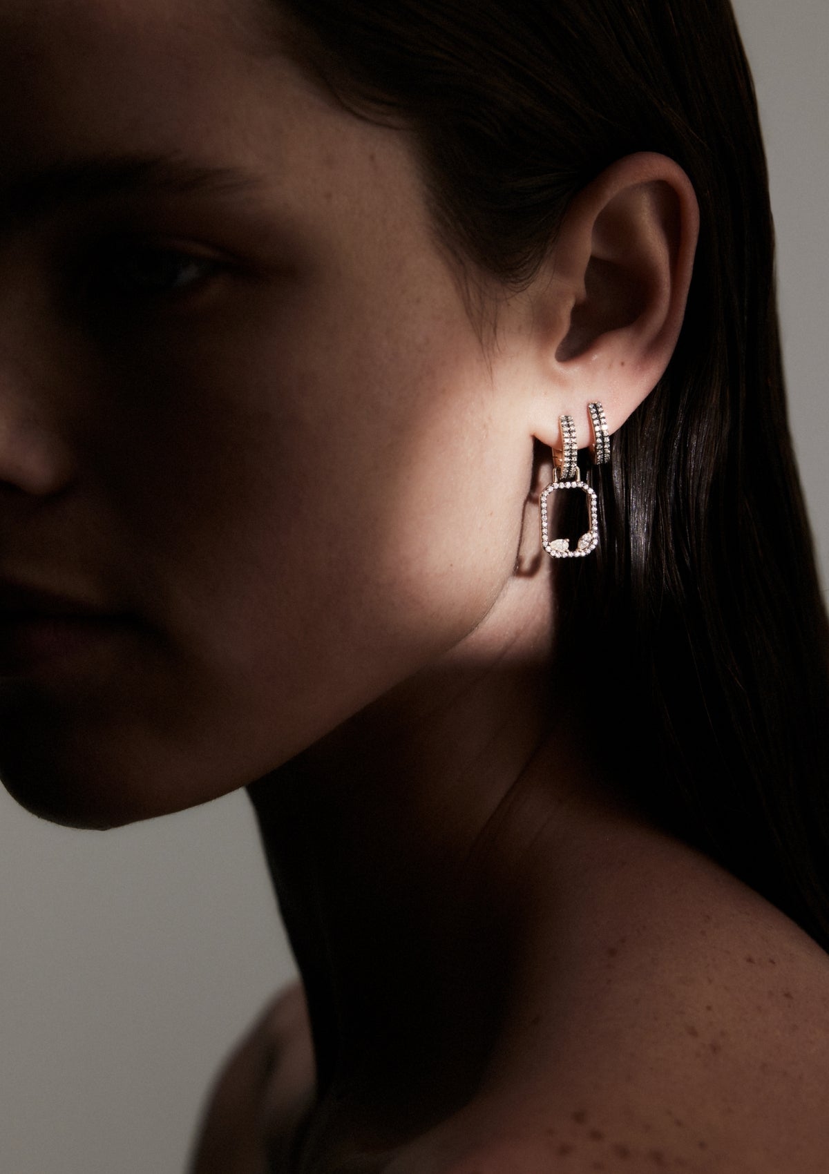woman with spotlight on her ear wearing geometric shaped gold earrings with round, pear and marquise diamonds