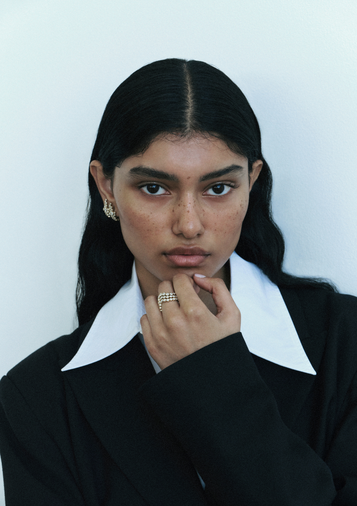 woman wearing a black outfit with a white collar and three sculptural diamond rings stacked on a finger against a light background