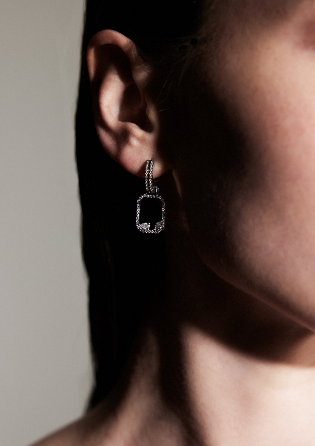 close up of woman's ear wearing rectangular geometrical drop earrings made with pear, round, marquise diamonds and diamond huggies.