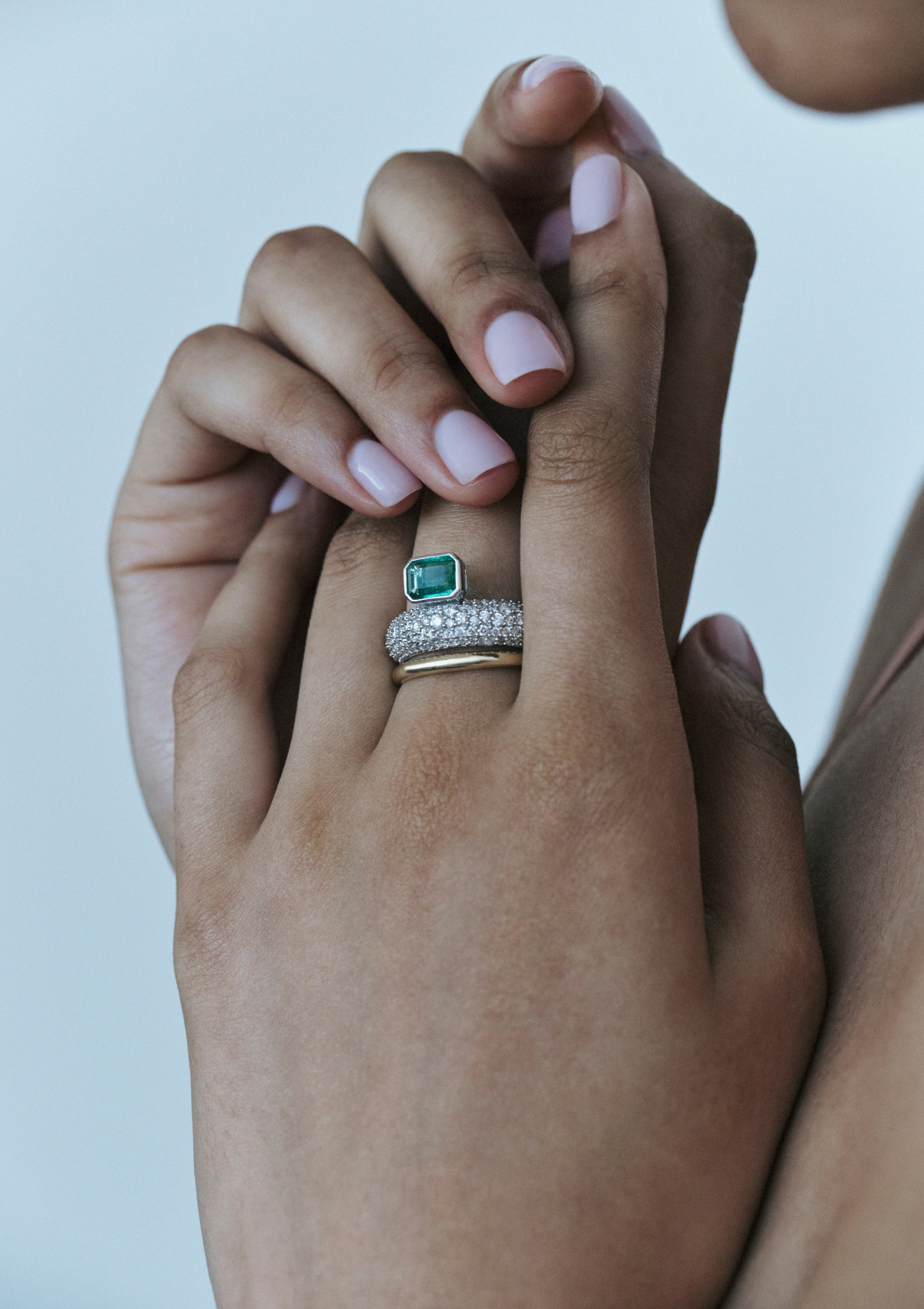 model wearing white gold ring with pave diamonds and an emerald sitting on top. and a yellow gold band below.