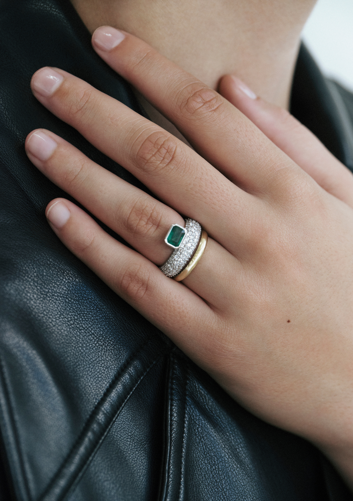 close up of hand wearing white gold ring with pave diamonds and an emerald sitting on top. and a yellow gold band below.