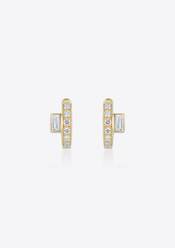 Gold diamond huggie earrings with baguette diamonds placed off-centre on a grey background